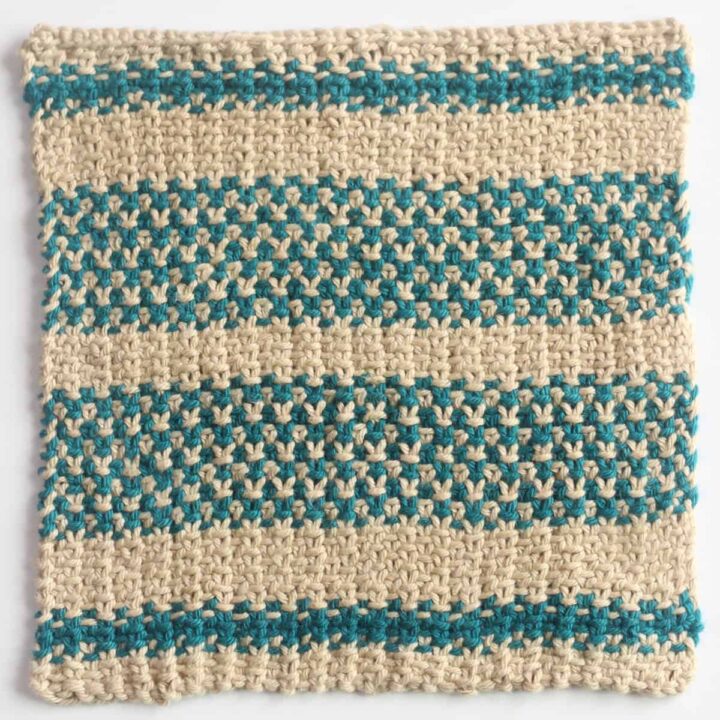 Small size dishcloth in the linen stitch knitted with tan and blue colored yarn.