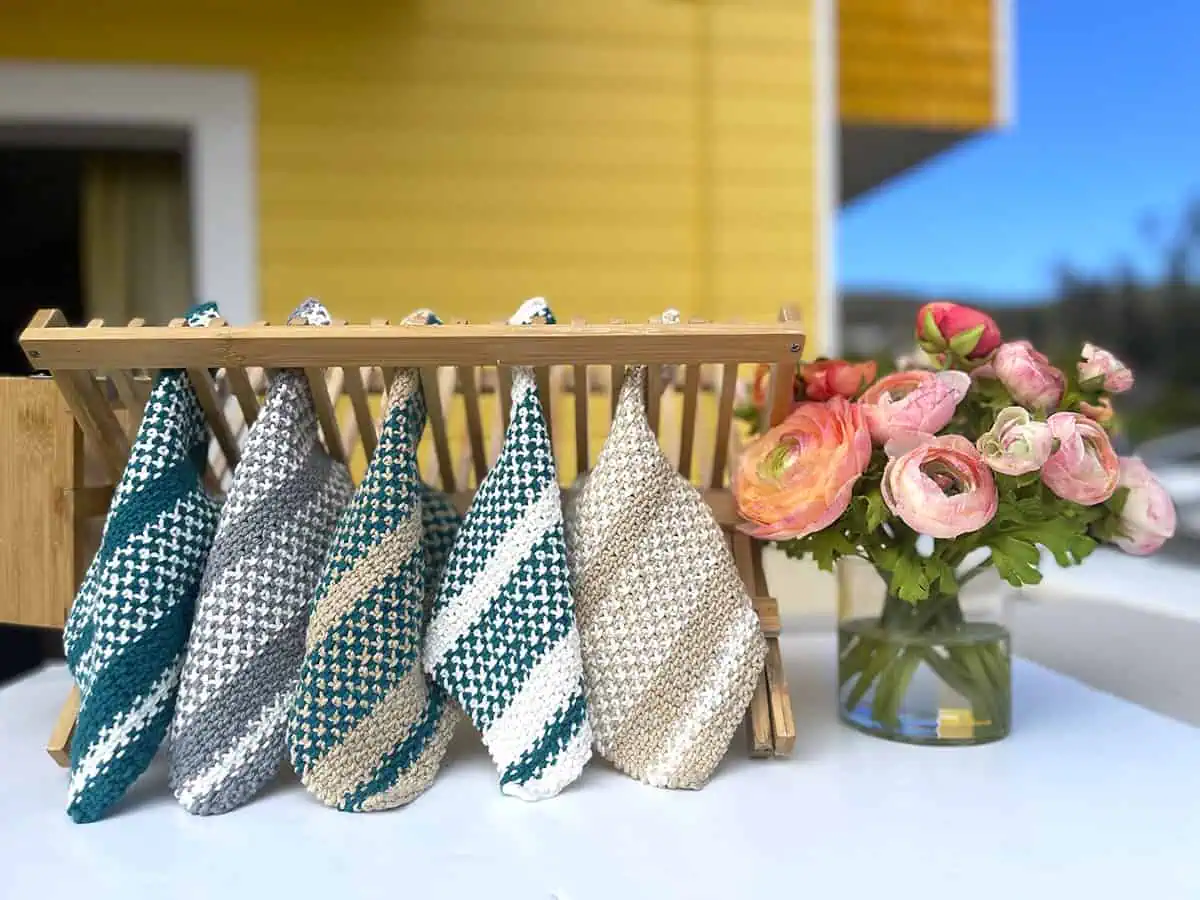 Five knitted dishcloths displayed on a dish rack with flowers.
