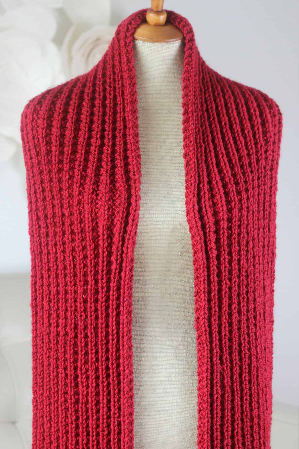 Seeded Rib Stitch Scarf knitted in red colored yarn draped on a mannequin.