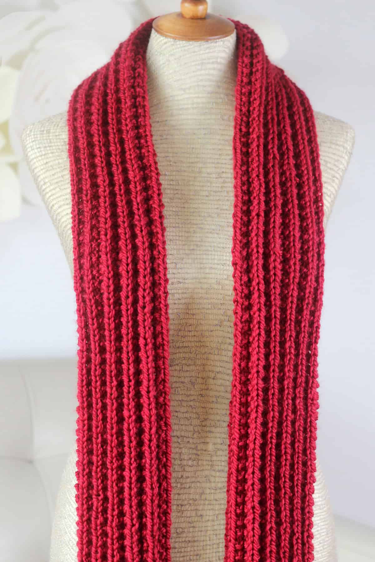 Seeded Rib Stitch Scarf folden once lengthwise knitted in red colored yarn.