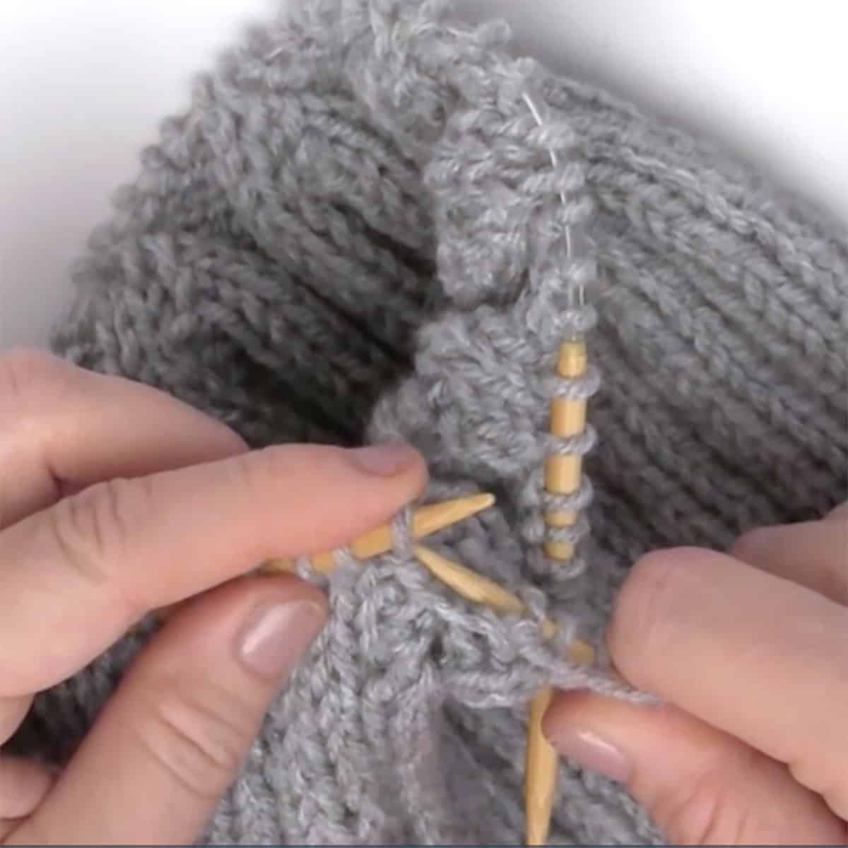 Hands switching from circular to double pointed knitting needles.