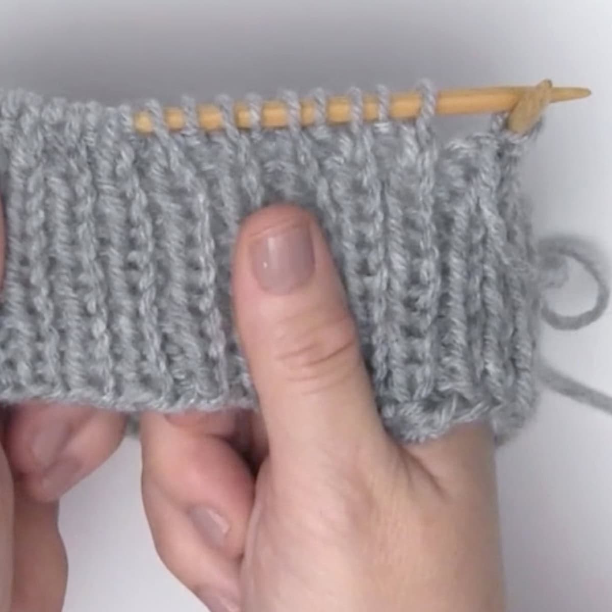 Hands knitting a hat brim on a circular needle.