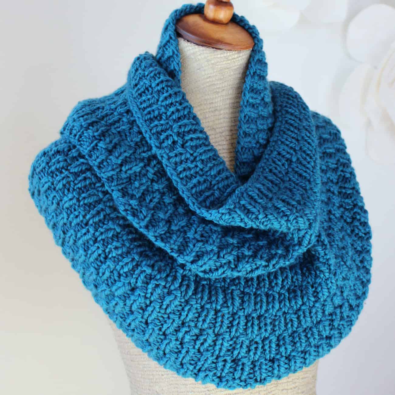 Blue knitted scarf in long raindrop stitch pattern wrapped around mannequin.
