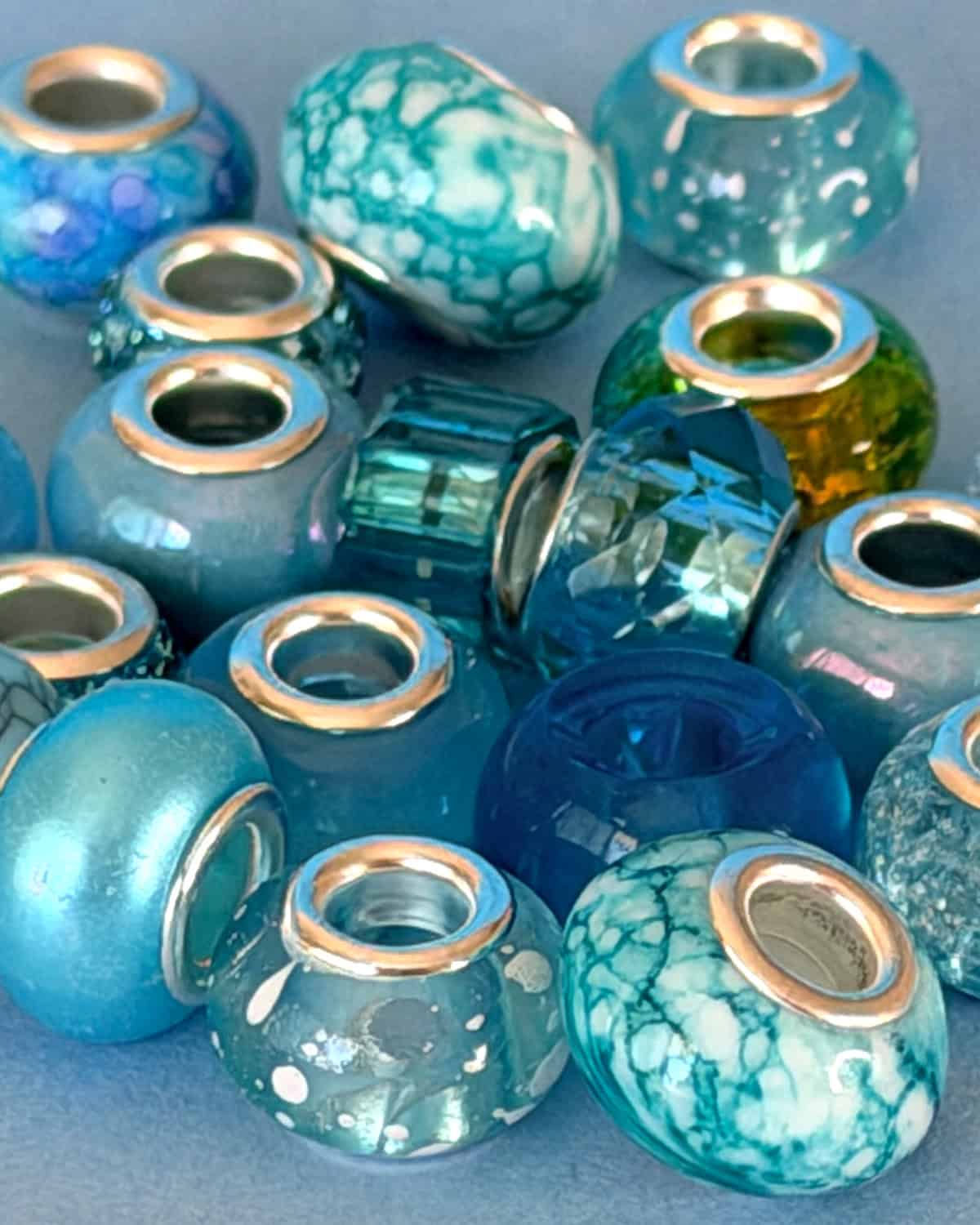 Close-up of assorted blue and turquoise glass beads with silver-lined holes, used to decorate knitted Christmas trees.