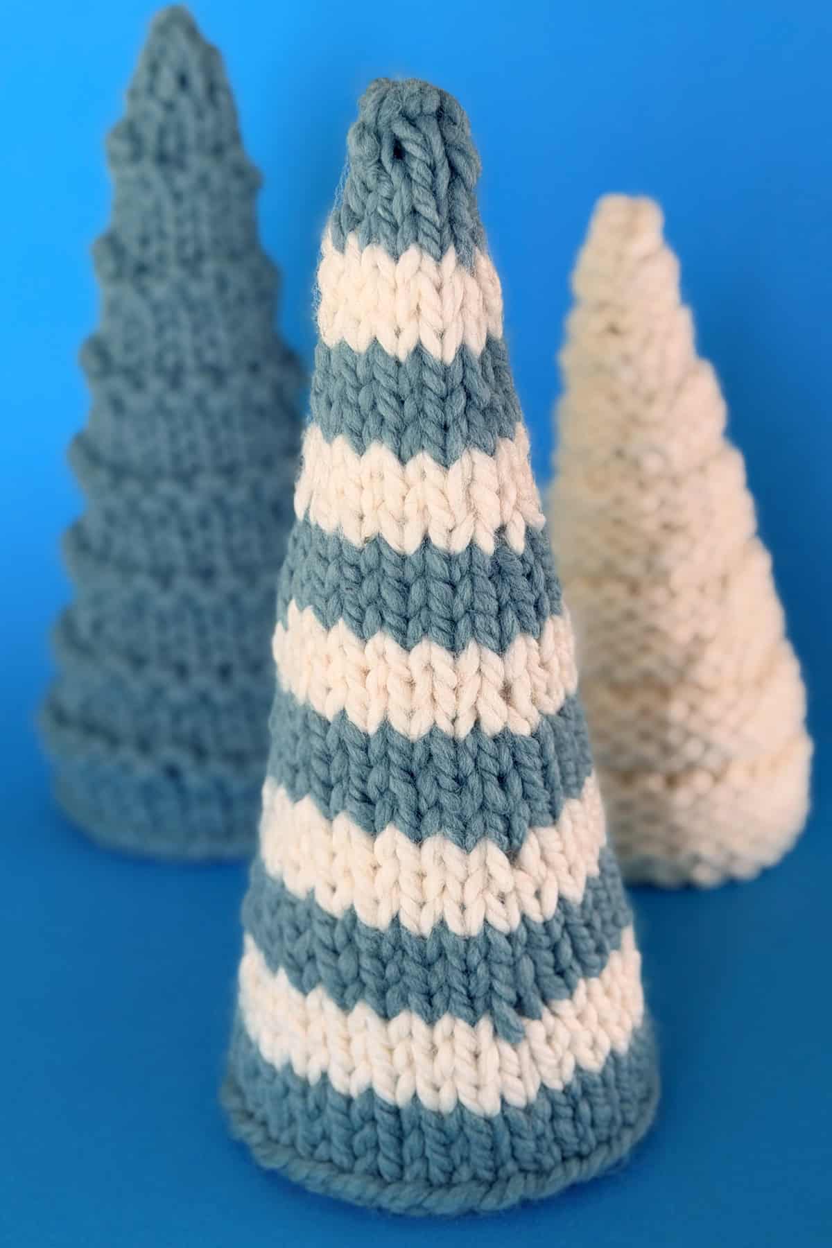 Knitted cone-shaped Christmas trees in blue and white stripes with textured variations displayed on a soft blue background.