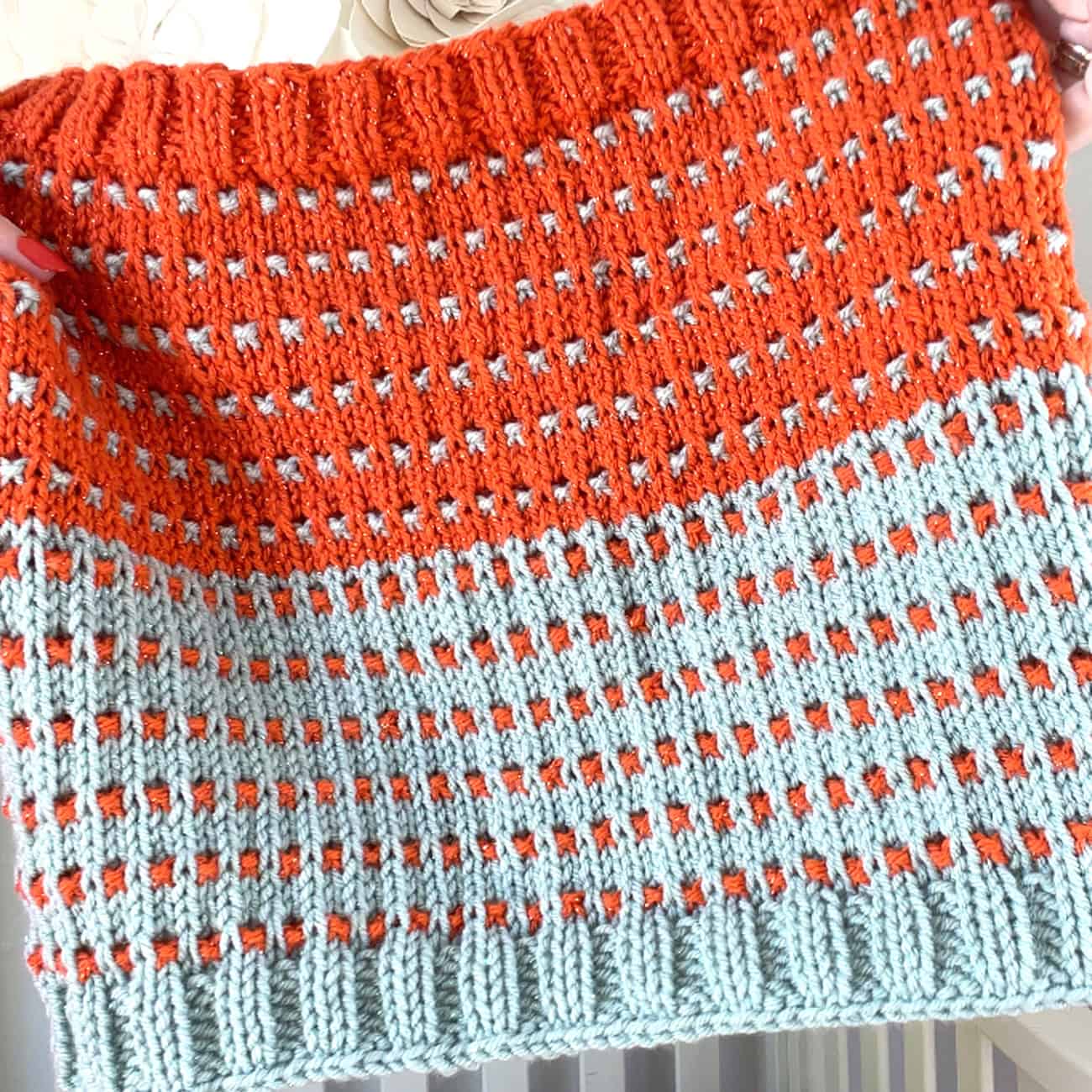 Close-up of the Soundtrack Cowl knit in sparkly orange and blue ice yarn, showing the textured rib and slip stitch pattern.