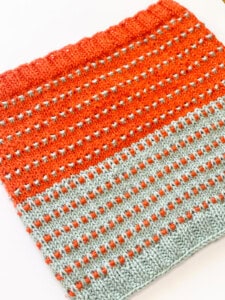 Knitted Soundtrack Cowl with orange sparkle yarn and gray contrast stripes, showing stitch detail.