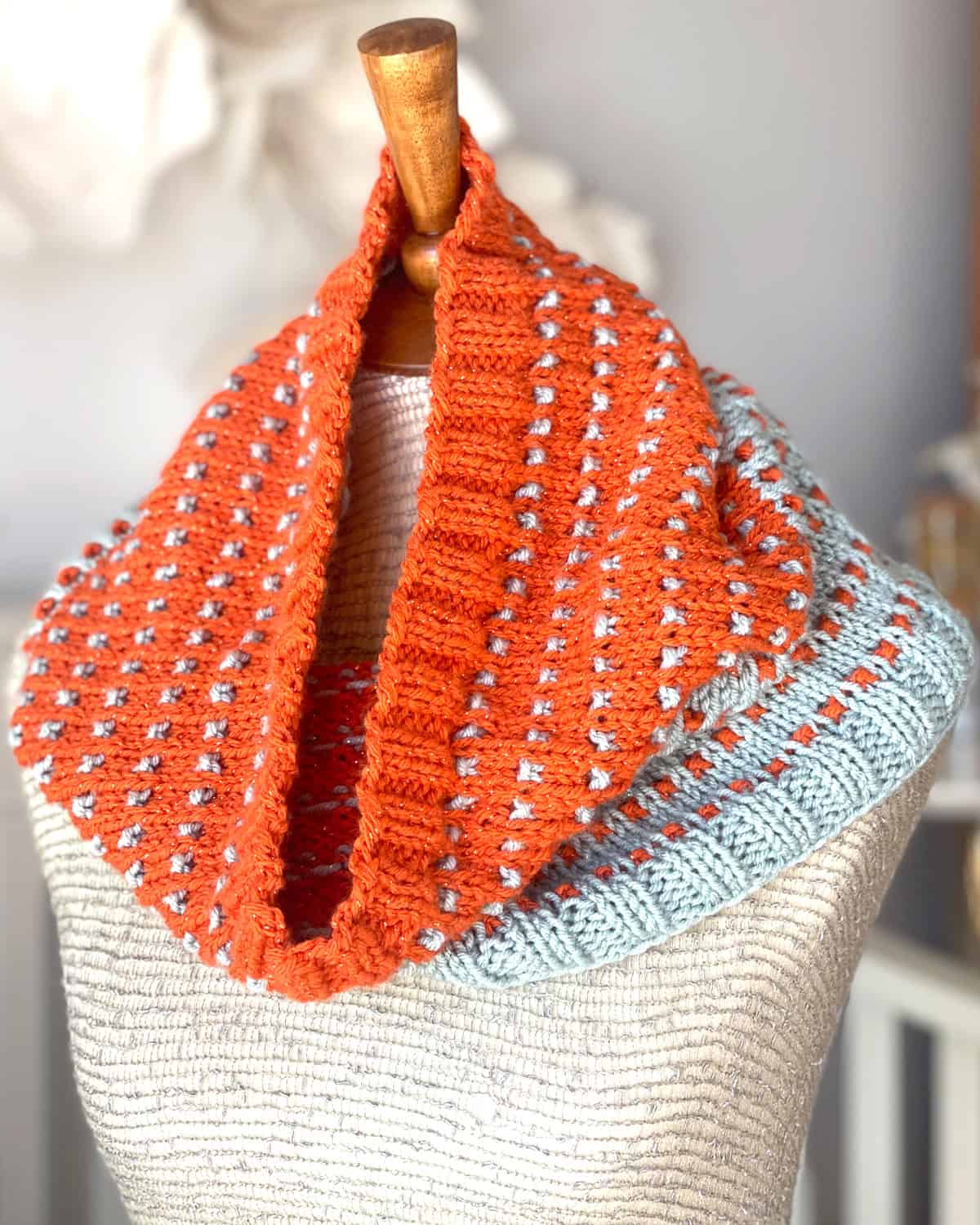 Hand-knit Soundtrack Cowl in sparkly orange and gray yarn, draped on a mannequin to show shimmer and texture.