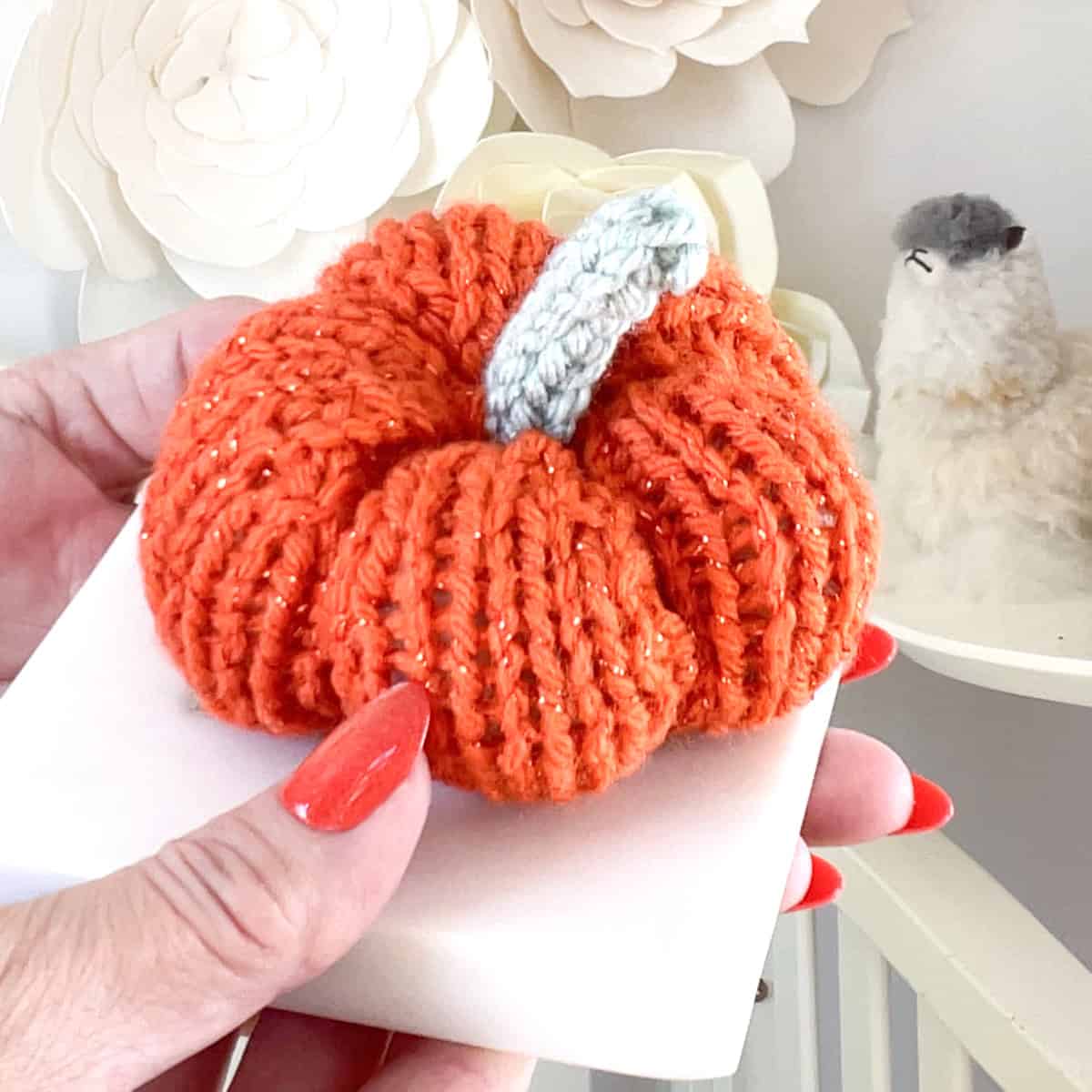 Hand holding a knitted pumpkin softie made with orange sparkly yarn and a gray stem.