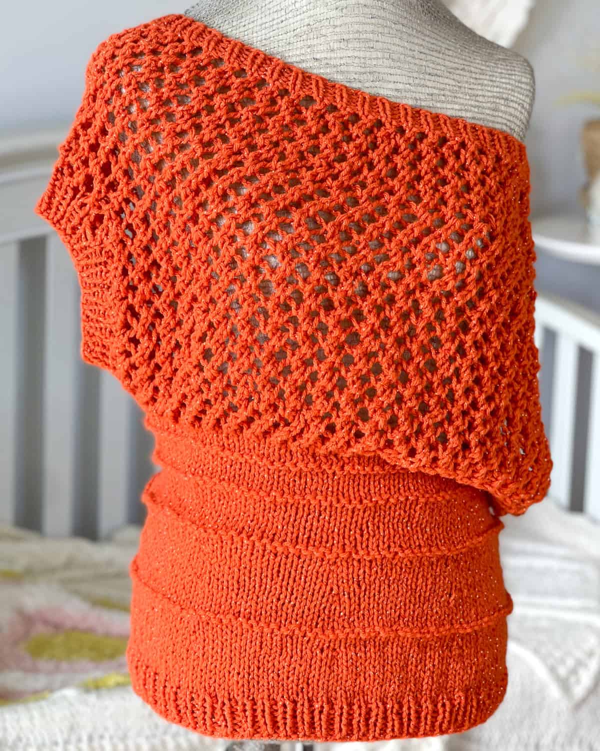 Knitted mesh lace top in orange sparkly yarn, displayed on a mannequin with openwork stitch pattern.