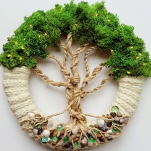 Knitted Tree of Life wreath with moss greenery and rope branches on white background.