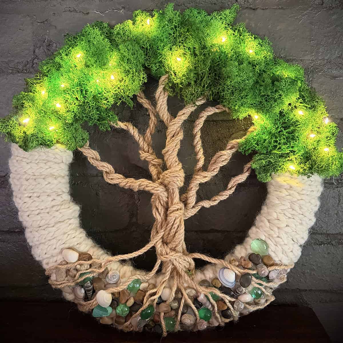 Handmade tree of life wall decor with lights, seashells, and knitted elements.