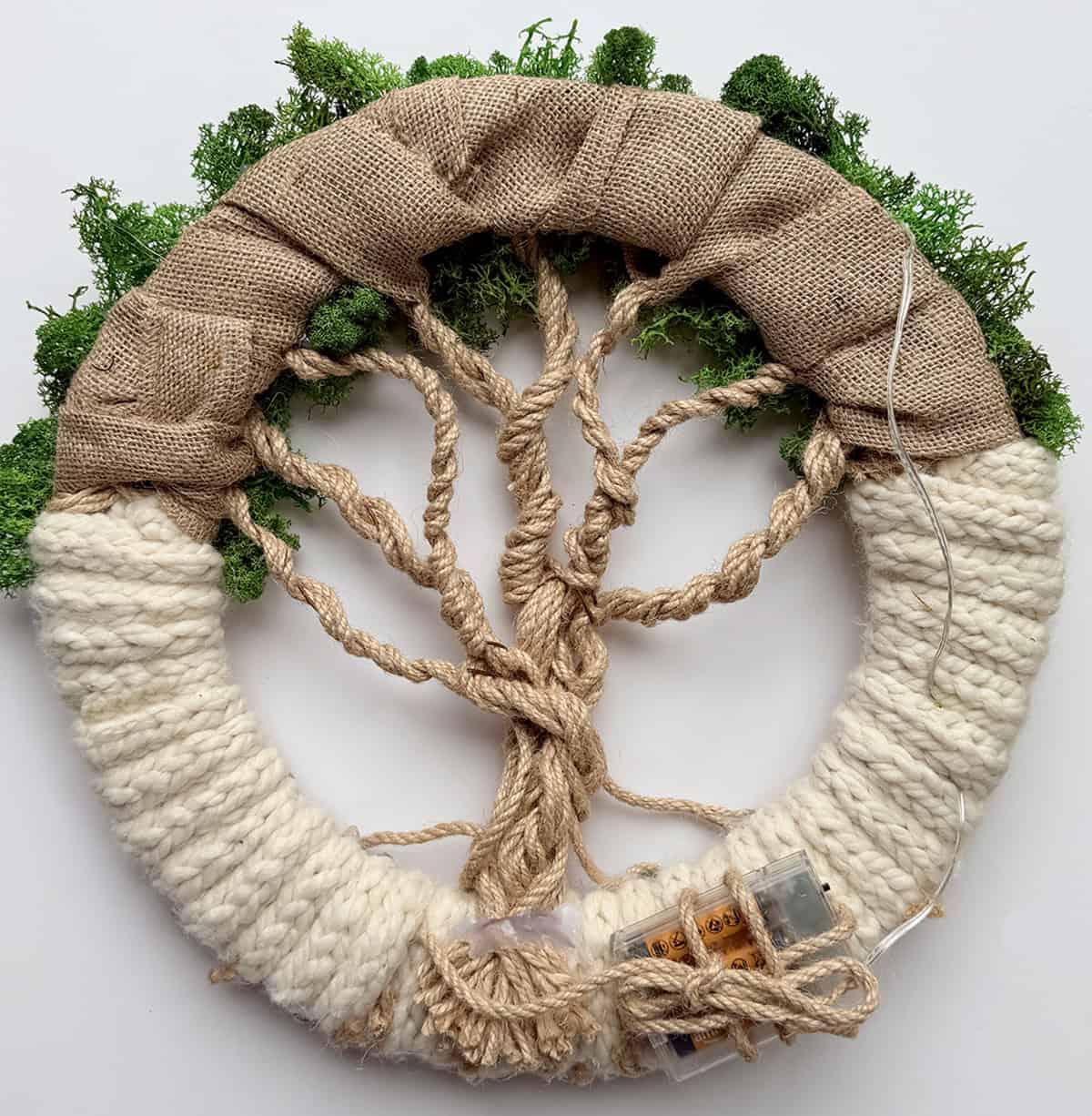 Back view of handmade Tree of Life wreath showing burlap base, jute twine branches, knitted i-cord wrap, fairy light battery pack, and wiring secured to the wreath frame.