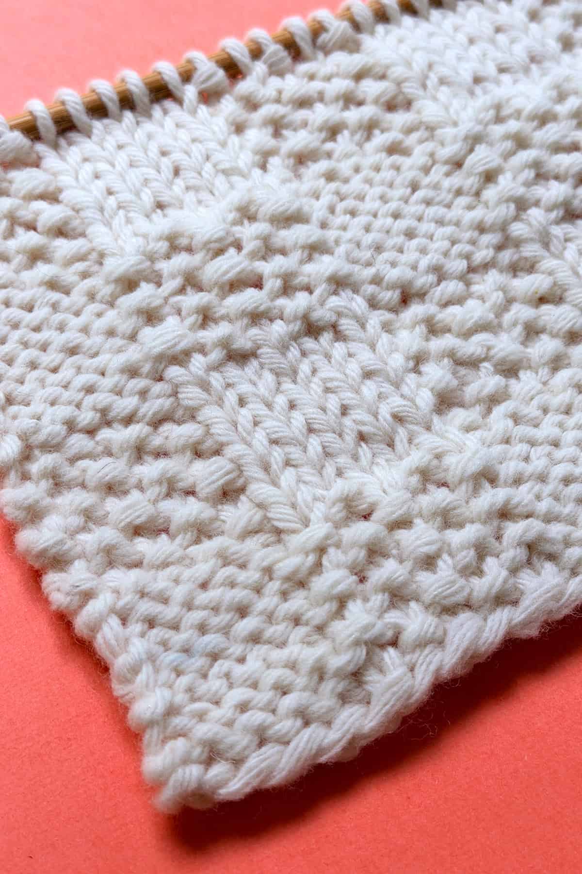 Angled view of Checkerboard Triple Weave Stitch edge on coral background, highlighting flat reversible texture.
