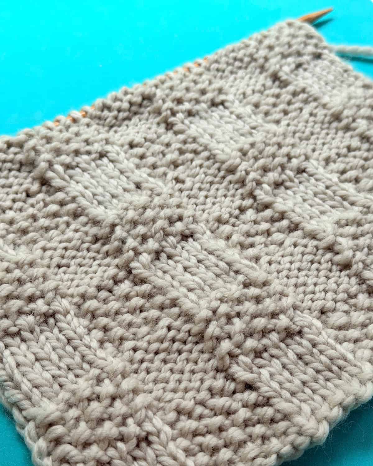 Angled Checkerboard Triple Weave Stitch swatch on teal background, emphasizing rib and seed blocks.