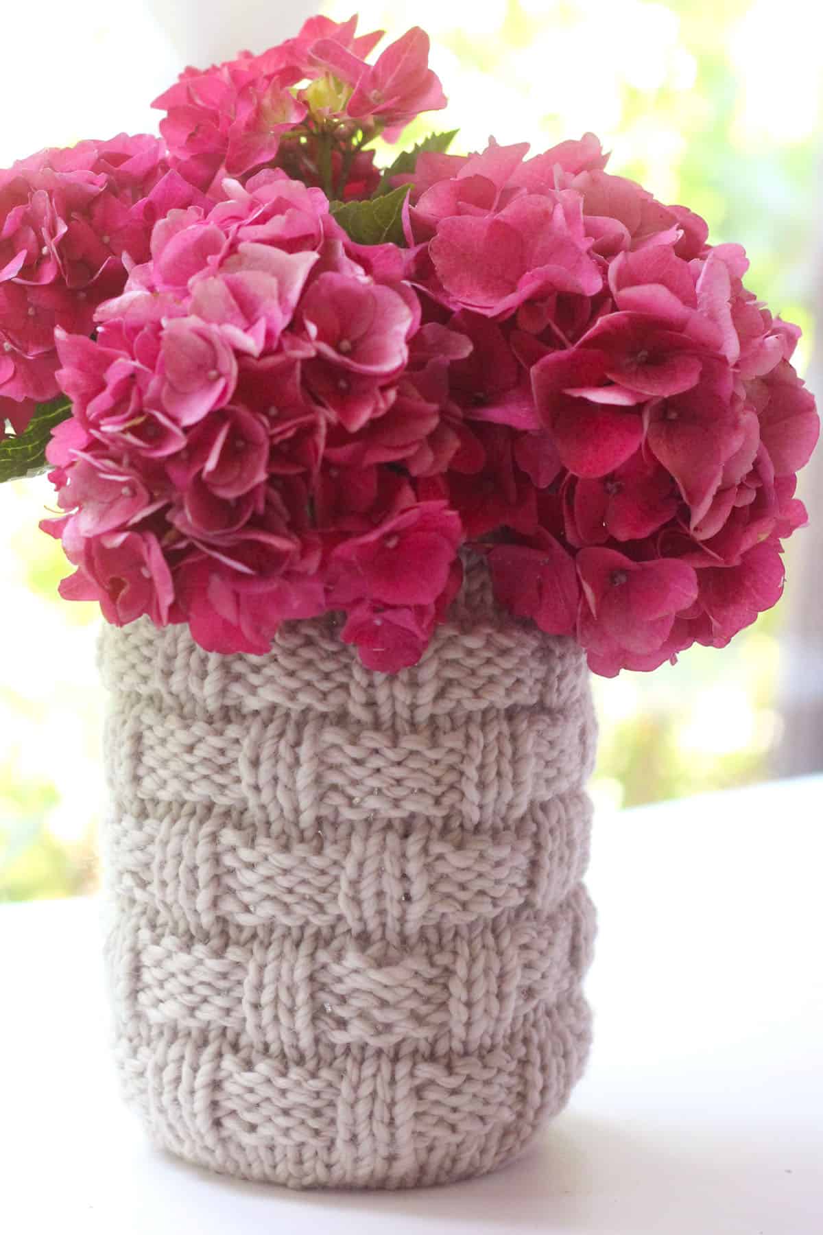 Knitted Basketweave Mason Jar Cozy holding bright pink hydrangea flowers.
