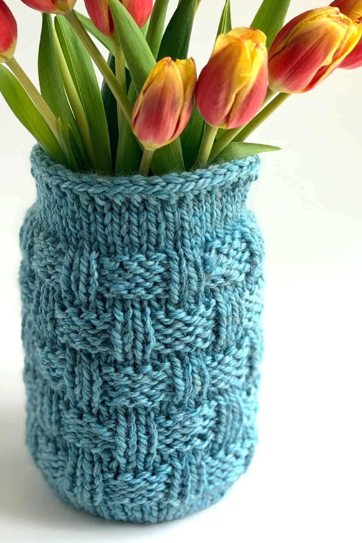 Basketweave Mason Jar Cozy Knitting Pattern in blue yarn holding pink and yellow tulips.