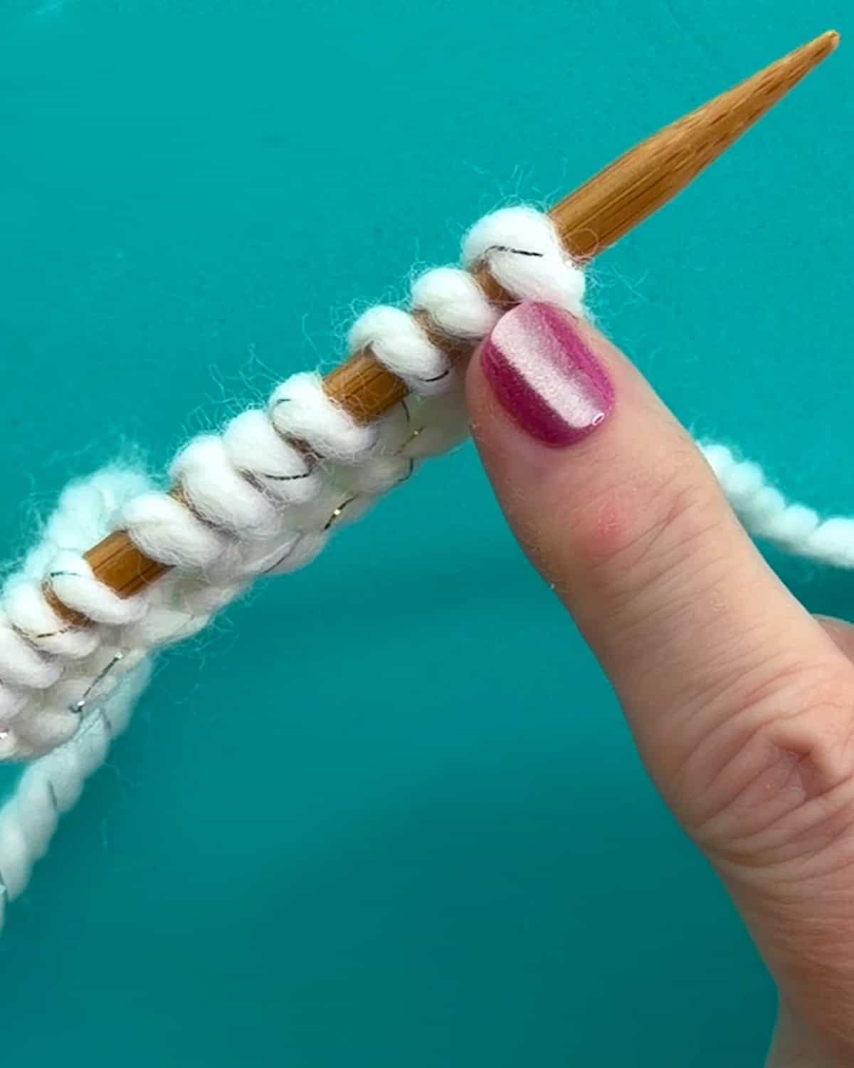 Close-up of the Knitted Cast On technique with white yarn on a wooden knitting needle.