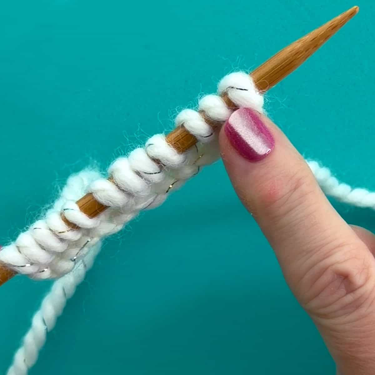 Knitted Cast On stitches worked onto a wooden knitting needle with white yarn.