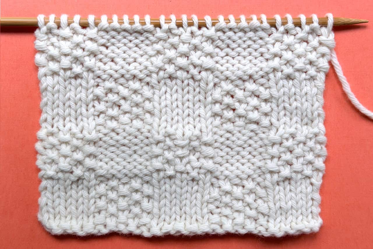Checkerboard Triple Weave Stitch swatch on coral background held on wooden needle, thumbnail image.