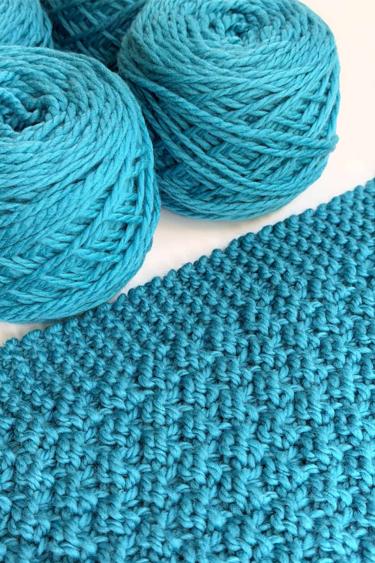 Close-up of turquoise textured knitting blanket swatch with matching blue yarn balls in a modern chunky knit pattern design.
