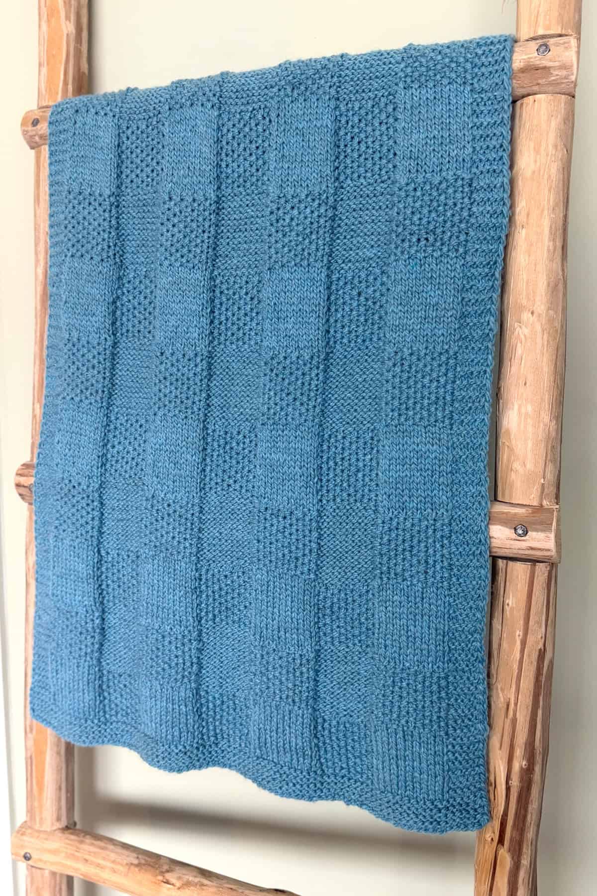 Blue Pescadero Harvest Blanket displayed on a wooden ladder with cozy checkerboard texture.