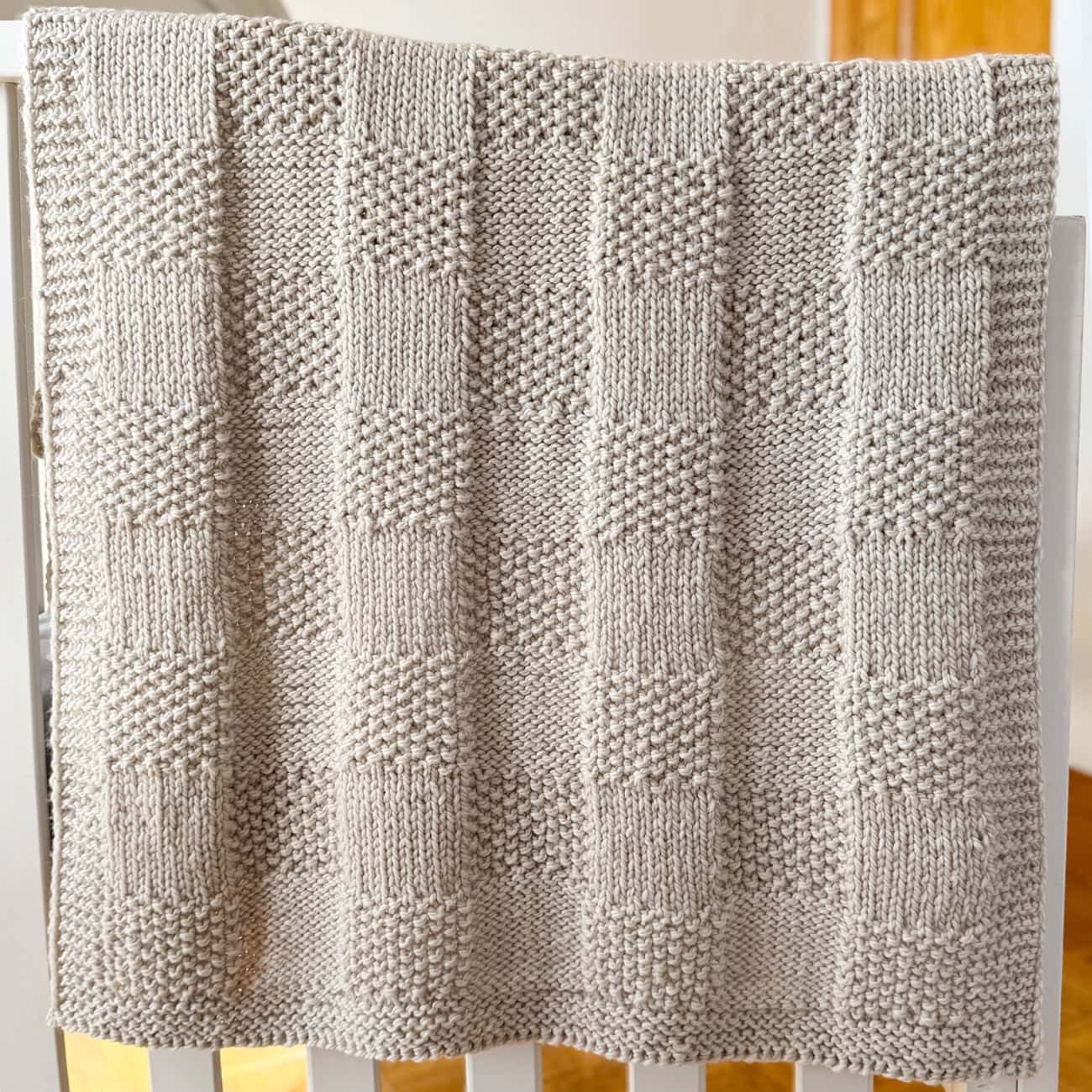 Feather grey Pescadero Harvest Blanket draped over a crib, showing the textured knit checkerboard design.