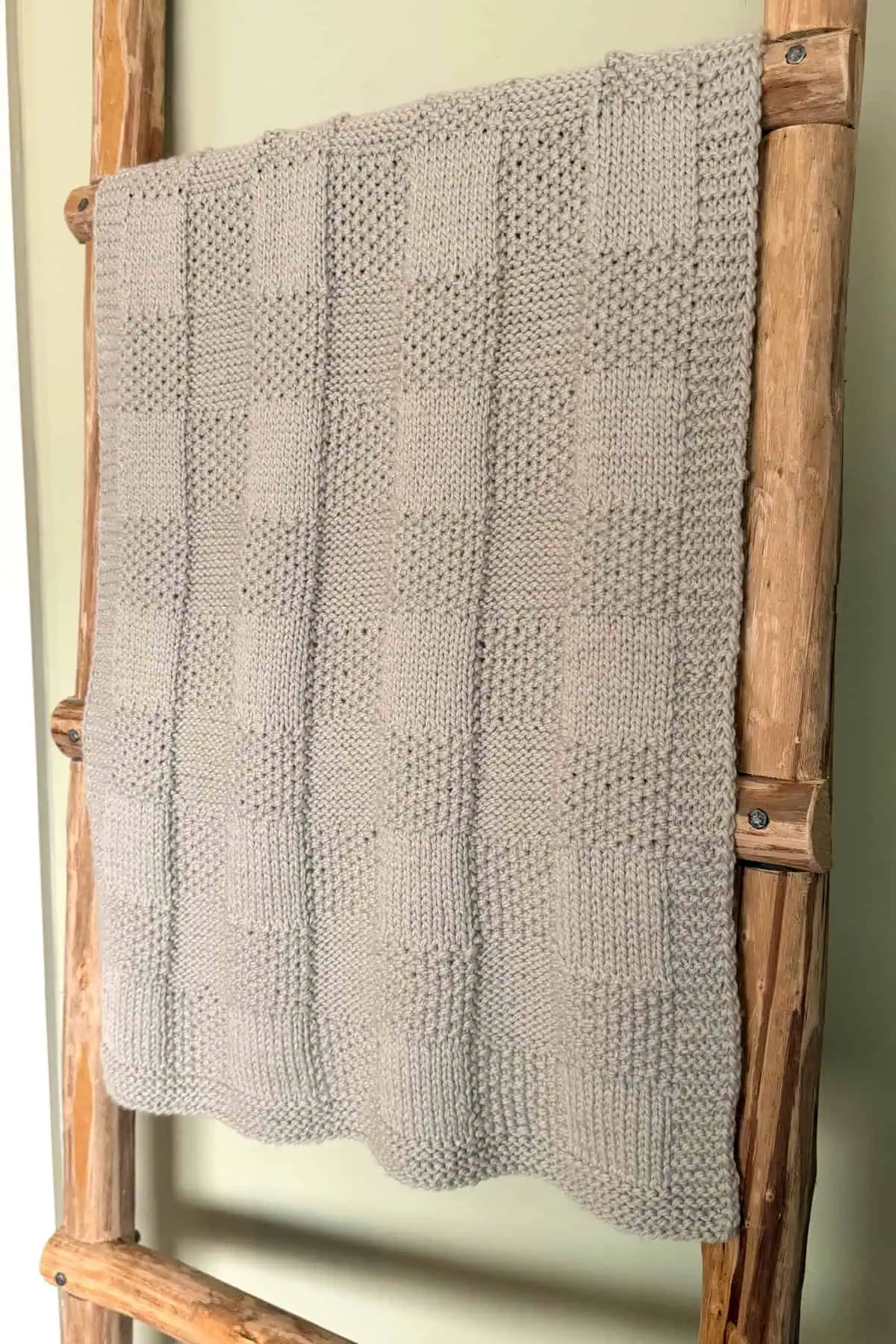 Feather grey Pescadero Harvest Blanket hanging on a wooden ladder with reversible checkerboard texture.