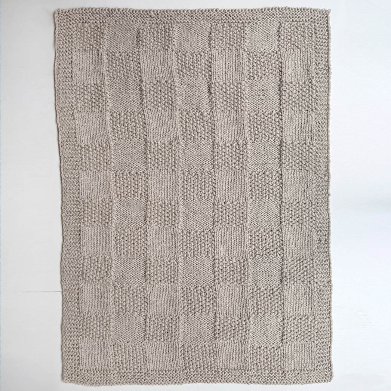 Full view of feather grey Pescadero Harvest Blanket laid flat, showing the checkerboard knit design.
