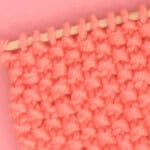 Knitted swatch in seed stitch texture with orange yarn and bamboo needle.