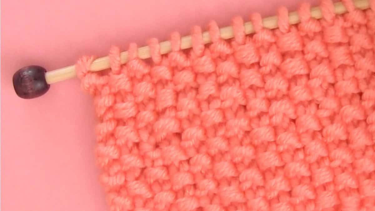 Knitted swatch in seed stitch texture with orange yarn and bamboo needle.
