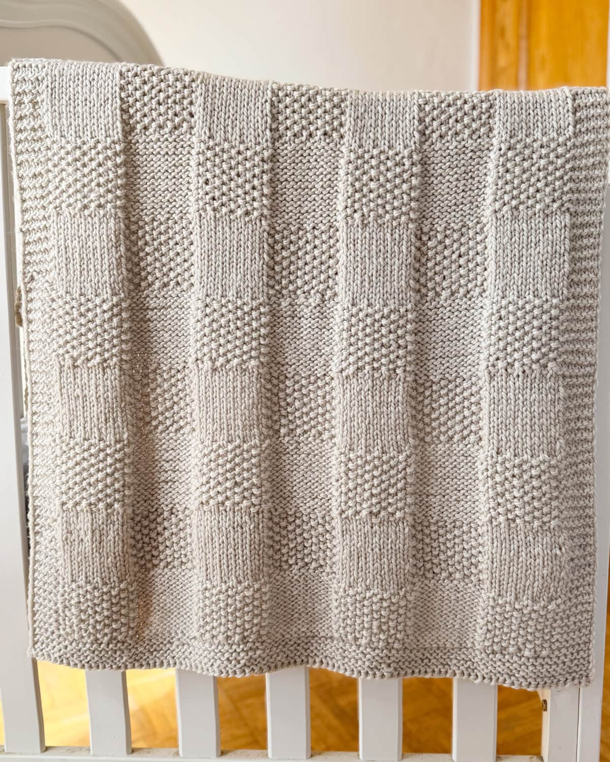 Feather grey Pescadero Harvest Blanket draped over a crib, showing the textured knit checkerboard design.